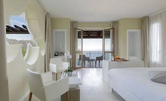 a white bedroom with a bed , a chair , and a door leading to a balcony overlooking the ocean at Villa Piedimonte