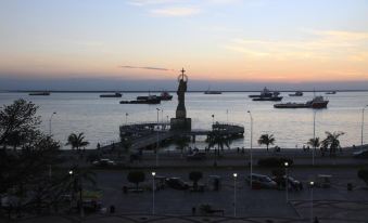 a statue of a woman stands on a pedestal in the middle of a harbor , with boats and vehicles nearby at Hotel del Parque