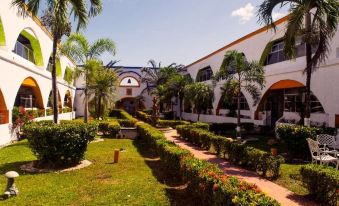 a white building with a red roof , surrounded by lush green plants and trees , under a clear blue sky at Hotel La Hacienda