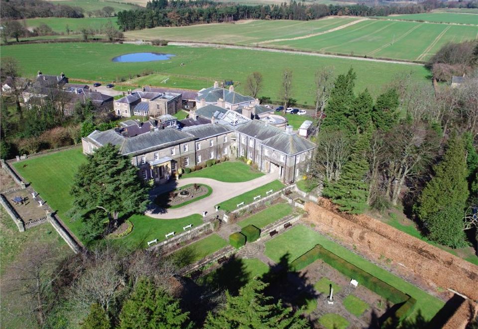 aerial view of a large mansion surrounded by green grass and trees , with a body of water nearby at Doxford Hall Hotel and Spa