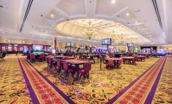 a large , well - lit casino with multiple dining tables and chairs , as well as a tv screen displaying the game at Casino Queen Hotel