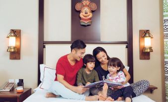 A family is sitting on a bed indoors, with the young daughter and father in front at Disney Explorers Lodge