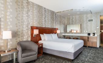 a large bed with white linens is situated in a room with gray walls and a gray armchair at Courtyard Newark-University of Delaware