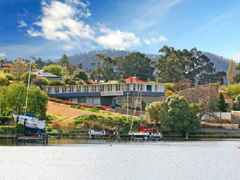 a large house with a red roof is situated on the shore of a lake , surrounded by trees and boats at Waterfront Lodge Motel