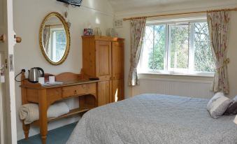 a cozy bedroom with wooden furniture , including a bed , dresser , and tv , along with a window and a door at Laburnum Cottage Guest House