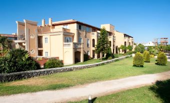 a large , beige - colored building with a stone wall and balconies is surrounded by trees and grass at Grupotel Club Turquesa Mar