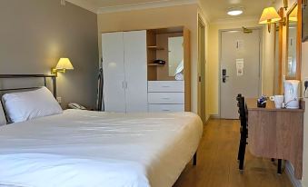 a hotel room with a large bed , white bedding , and a desk , along with other furniture such as a door and cabinets at 247Hotel.Com