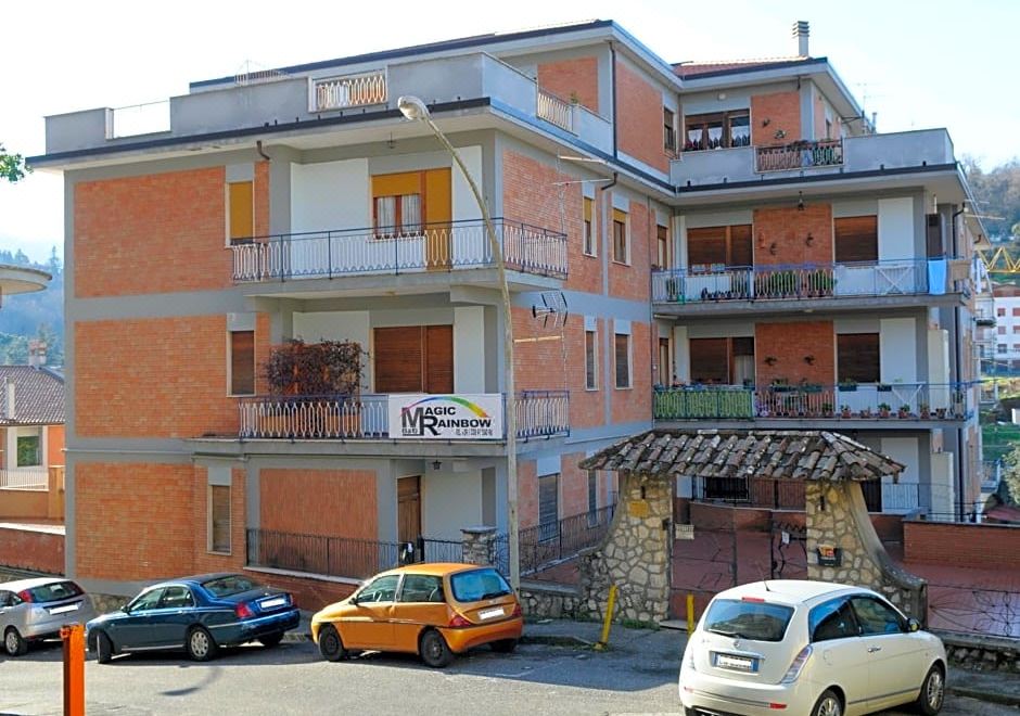 a brick apartment building with multiple balconies and cars parked in front , under a clear blue sky at Magic Rainbow