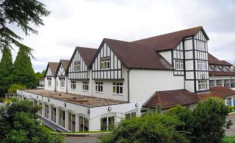 a large , white building with brown roofs and windows is surrounded by trees and bushes at Buckatree Hall Hotel