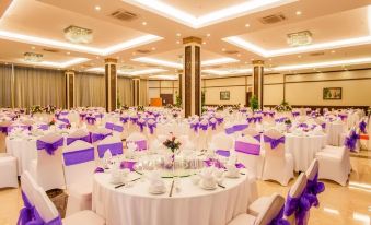 a large banquet hall with multiple tables covered in white tablecloths and adorned with purple flowers at Muong Thanh Grand Quang Nam