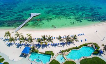 a tropical beach with clear blue water , palm trees , and umbrellas , as well as several lounge chairs and umbrellas at Wyndham Reef Resort Grand Cayman