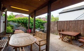 a wooden patio set with a table and benches is surrounded by greenery , and a house in the background at The Howard Arms