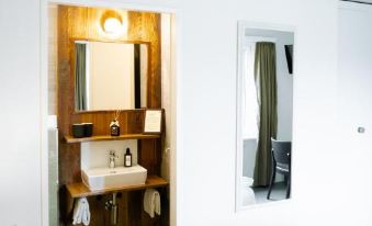 a bathroom with a wooden shelf holding towels and a mirror above the sink , reflecting the room 's interior at Alpenblick Weggis - Panorama & Alpen Chic Hotel
