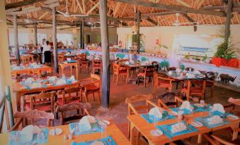 a restaurant with wooden tables and chairs , blue napkins , and a person at the end of the table at VOI Wildlife Lodge