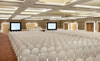 a large , empty conference room with rows of white chairs and multiple screens on either side at Hyatt Centric Janakpuri New Delhi