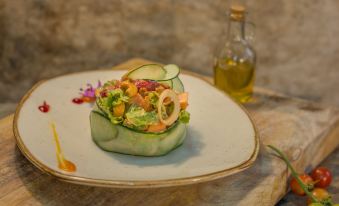 a plate with a salad topped with cucumber and other ingredients , next to a bottle of olive oil at La Tigra Rainforest Lodge