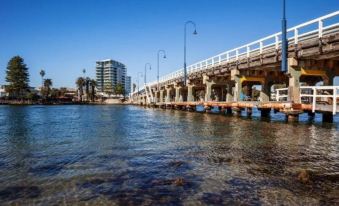 a wooden pier extending into the water , with a tall building in the background and street lights illuminating the area at C Mandurah Apartment Resort