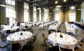 a large , well - lit room with numerous round tables and chairs set up for a banquet or special event at Steigenberger Braunschweig