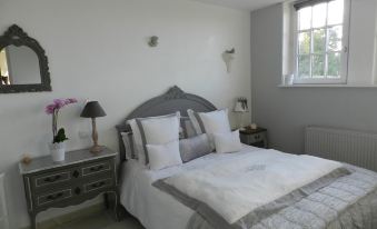 a cozy bedroom with a white bed , gray and white bedding , and a wooden nightstand at Le Pressoir