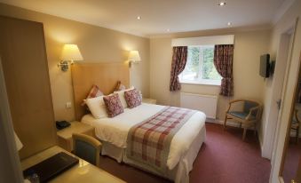 a large bed with a wooden headboard and plaid blanket is in the middle of a room at Little Silver Country Hotel