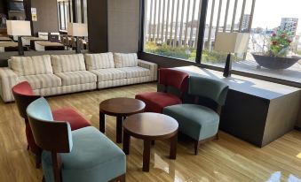 a modern living room with wooden floors , white sofas , and colorful chairs arranged around a coffee table at Meitetsu Inn Kariya