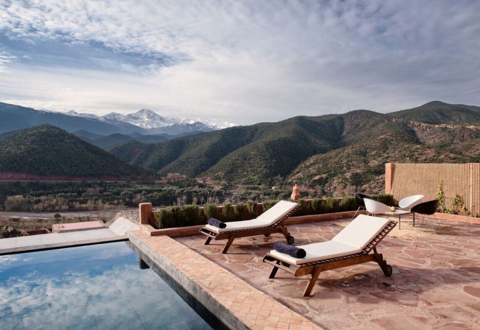 a large pool with two lounge chairs situated on a patio overlooking a mountainous landscape at Kasbah Bab Ourika