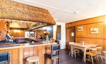 a restaurant with wooden walls and a thatched roof , featuring a bar and several tables at Three Horseshoes Inn