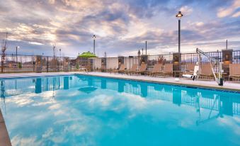 a large outdoor swimming pool surrounded by lounge chairs and umbrellas , with the sun setting in the background at Hyatt House Provo/Pleasant Grove