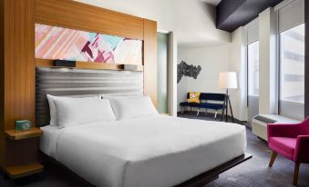a modern bedroom with a white bed , a couch , and a tv . the room is well - lit , and the furniture is well - at Aloft Leawood-Overland Park