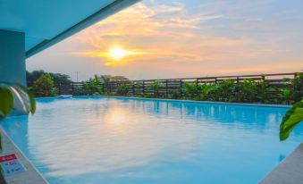 a large swimming pool with a wooden deck and greenery on the side , overlooking a beautiful sunset at Swiss-Belhotel Serpong
