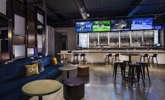 a modern bar with a long counter and multiple televisions displaying sports events , surrounded by comfortable seating at Aloft Little Rock West
