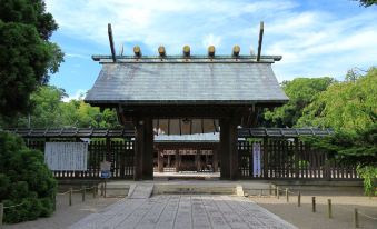 a large wooden gate with a pointed roof , surrounded by trees and a stone walkway at Art Hotel Miyazaki Sky Tower