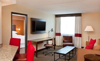 a hotel room with a television , couch , desk , and chair , as well as a bed in the background at Four Points by Sheraton Saginaw