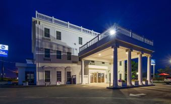 "a large white building with a balcony and columns is illuminated at night , and a sign reading "" entrance "" in front of it" at Best Western White House Inn
