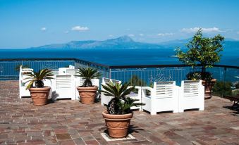 a terrace with white planters and red - brick flooring , overlooking the sea and mountains under a clear blue sky at Hotel Martino