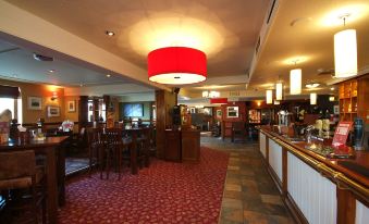 a dimly lit restaurant with multiple dining tables , chairs , and a bar area , as well as a red carpet on the floor at Premier Inn Blackpool Airport