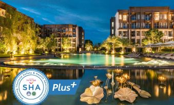 a serene nighttime scene at a resort , with the hotel building illuminated and a large swimming pool surrounded by greenery at Divalux Resort and Spa Bangkok, Suvarnabhumi Airport-Free Shuttle