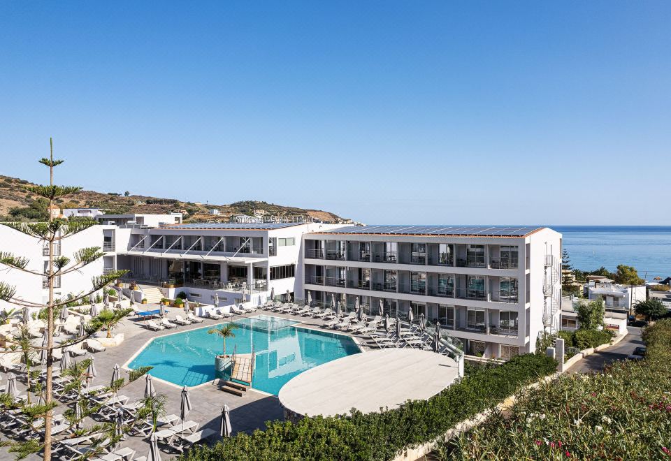 a large hotel with a swimming pool surrounded by chairs and umbrellas , located near the ocean at Atali Grand Resort