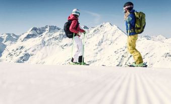 two people are skiing on a snow - covered slope , with one person in the foreground and the other in the background at Hotel Post