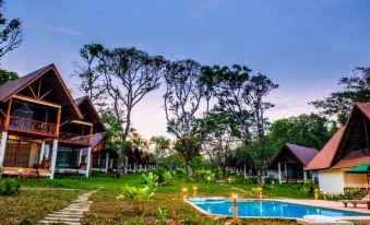 a serene scene of a wooden cabin surrounded by trees , with a swimming pool in the foreground at Phayamas Private Beach Resort and Island Brew - Adults Only