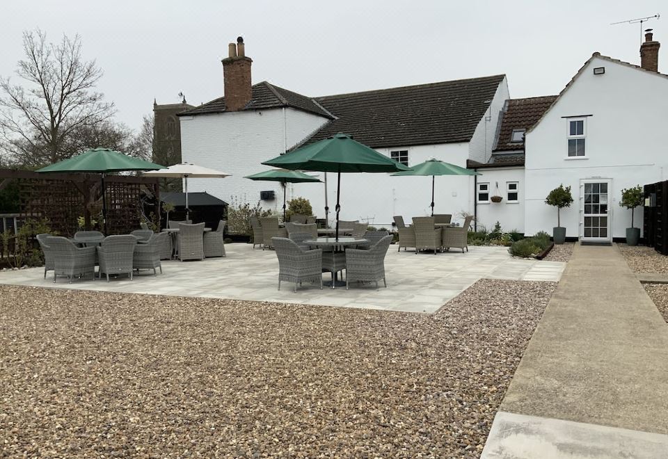 a courtyard with a variety of outdoor furniture , including umbrellas and tables , surrounded by a white house at The Red Lion Inn