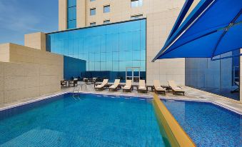 a large swimming pool with lounge chairs and a blue umbrella in front of a building at Hilton Garden Inn Tabuk