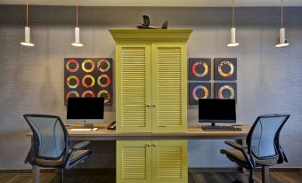 a room with two computer desks , each equipped with a computer monitor and keyboard , as well as a yellow cabinet at Home2 Suites by Hilton Springdale Cincinnati