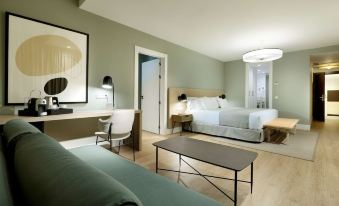 a modern hotel room with a green wall , white bed , and a dining table , as well as a living area with a couch and tv at Barceló Oviedo Cervantes