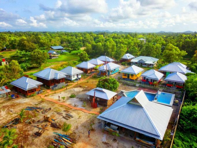 aerial view of a village surrounded by green trees , with a small village in the background at Rock and Wreck Dive Resort