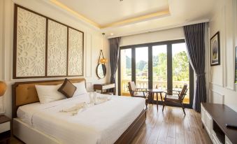 a large bed with white linens is in a room with wooden floors and a sliding glass door at Doan Gia Resort Phong Nha