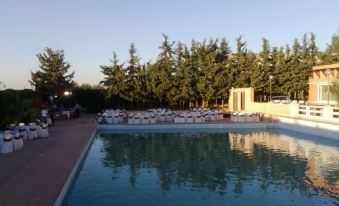 a large outdoor pool surrounded by tables and chairs , with trees in the background and a building in the distance at Pomaria