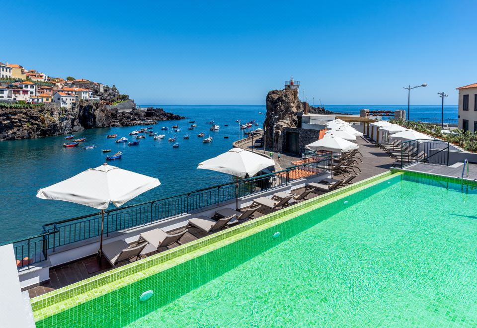 a rooftop pool overlooking a marina filled with boats , surrounded by white umbrellas and green walls at Pestana Churchill Bay