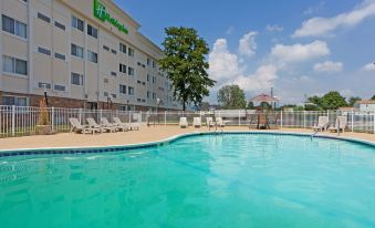 a large outdoor swimming pool surrounded by chairs and umbrellas , with a holiday inn hotel in the background at Wyndham Garden Dover