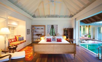 a large bedroom with a wooden bed , red and white pillows , and a door leading to a balcony at Naladhu Private Island Maldives